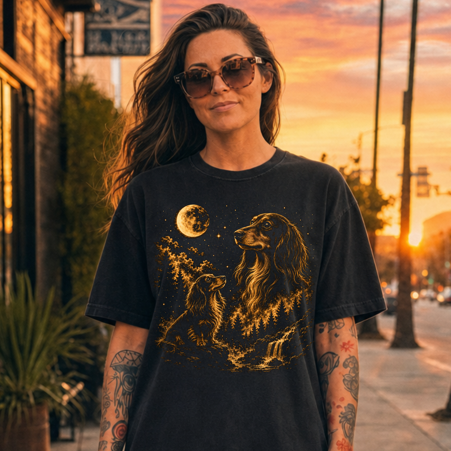 Woman wearing a black t-shirt with a graphic design of a Long Haird Dachshund dog and moon, standing outdoors during sunset.